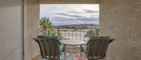 Un balcon avec deux chaises et une table, une vue sur un immeuble et des palmiers, et un tapis à motifs.