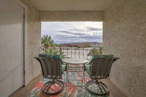 A balcony with two chairs and a table, a view of a building and palm trees, and a patterned rug. - Las Palmas Resort #1642 | All-Inclusive Amenities (Saint George)