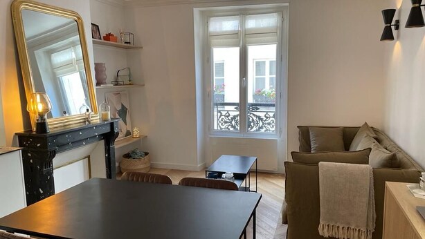 Ett vardagsrum med ett matbord, stolar, en soffa, en öppen spis och ett stort fönster med utsikt över balkongen.