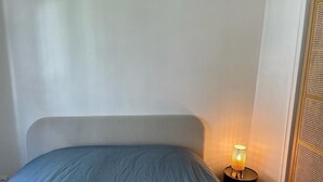 Ett sovrum med en säng, ett nattduksbord med en lampa och en vävd avskärmning.