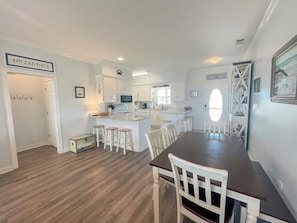 A modern kitchen with white cabinets, a central island with stools, and a dining area with a dark wooden table and white chairs.