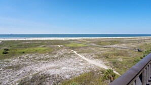 A coastal landscape with a beach, grassy areas, and a wooden boardwalk.