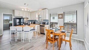 Una cocina moderna con armarios blancos, una isla central y un comedor con sillas y mesa de madera.