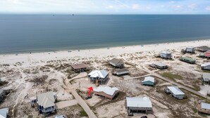 Luchtbeeld van een kustgemeenschap met huizen, waarvan sommige op palen staan, en een zandstrand op de voorgrond.