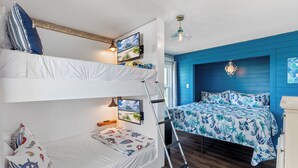Een slaapkamer met stapelbed, een ladder, een bed met een blauw bloemenbedover en een tv aan de muur.