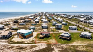Luchtbeeld van een kustgebied met woonhuizen, waarvan sommige voorzien zijn van veranda's en terrassen, en een strand op de achtergrond.