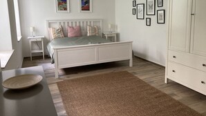 Un dormitorio con cama, mesitas de noche, armario y cuadros en la pared.