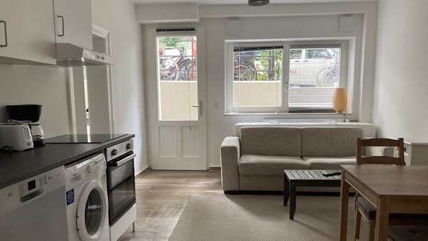 Un espacio habitable compacto con kitchenette, lavadora, sofá y comedor.
