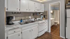 A compact kitchen with white cabinets, a stove, and a sink. - Krystal Villa East 303- Nice, Central to Town (Mammoth Lakes)