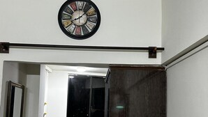 A wall-mounted clock with a classic design, a door frame, and a door leading to a dark room.