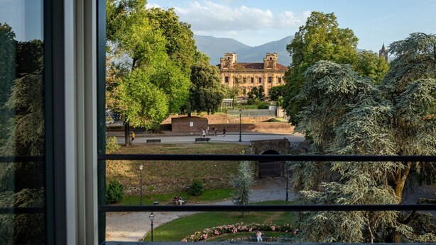 A view of a historic building with a large central courtyard, surrounded by trees and a mountain backdrop. - Residence  Thym N3003 (Lucca)