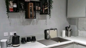 A modern kitchen with a white countertop, a sink, and a built-in oven. There are black shelves above the countertop holding various kitchen items. - Remarkable 3-bed House in Chelmsford (Chelmsford)