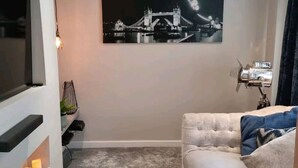 A modern living room with a large flat-screen TV, a cozy sofa, a framed picture of a bridge, and a vintage camera on a tripod. - Remarkable 3-bed House in Chelmsford (Chelmsford)