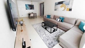 Ein modernes Wohnzimmer mit Sofa, Couchtisch und Fernseher. Es gibt einen Essbereich mit Stühlen und einem Tisch.