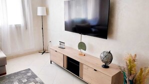 Ein modernes Wohnzimmer mit einem flachbildfernseher an der Wand, einem Holz-TV-Möbel mit Globus und Kalender, einer Stehlampe und einem grauen Teppich.