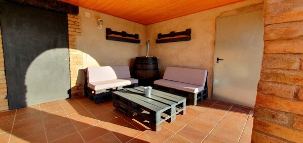 A rustic outdoor seating area with wooden benches and a table, a barrel, and a door.