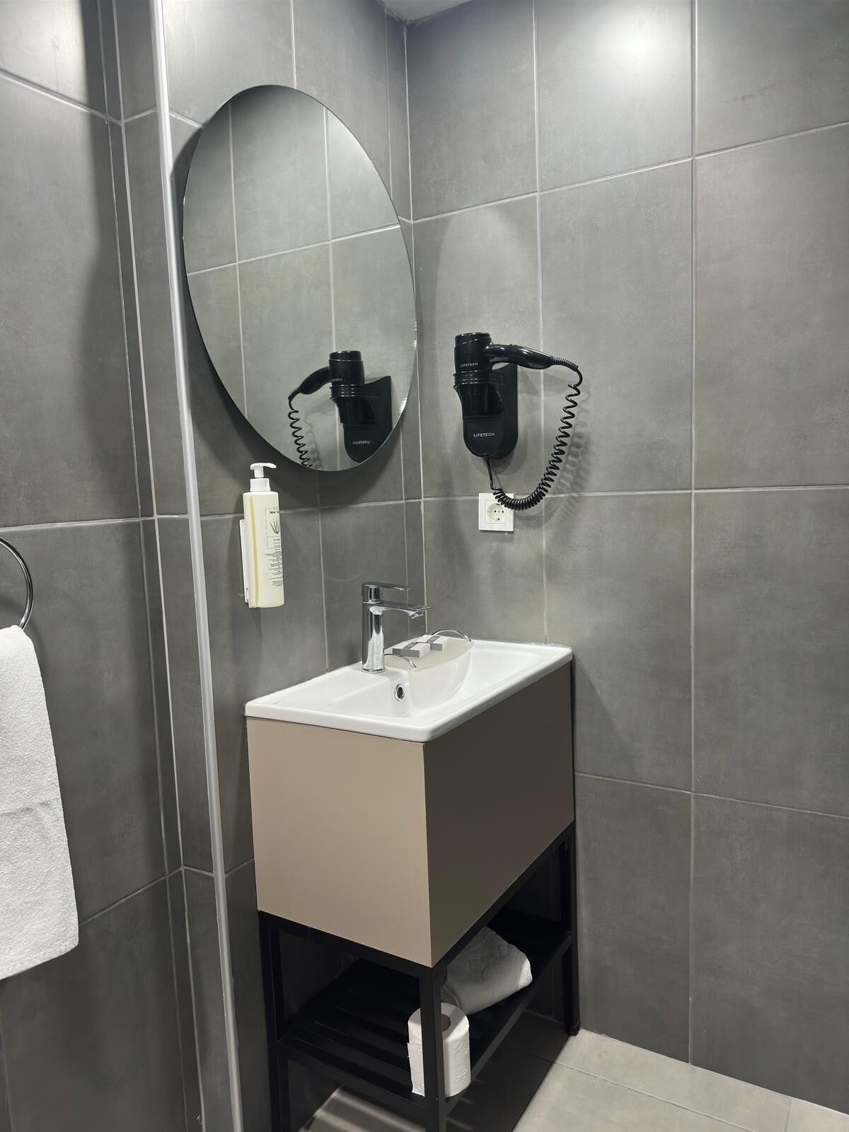 A modern bathroom with a rectangular sink, a round mirror, and a hairdryer mounted on the wall.
