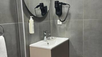 Un baño moderno con un lavabo rectangular, un espejo redondo y un secador de pelo montado en la pared.