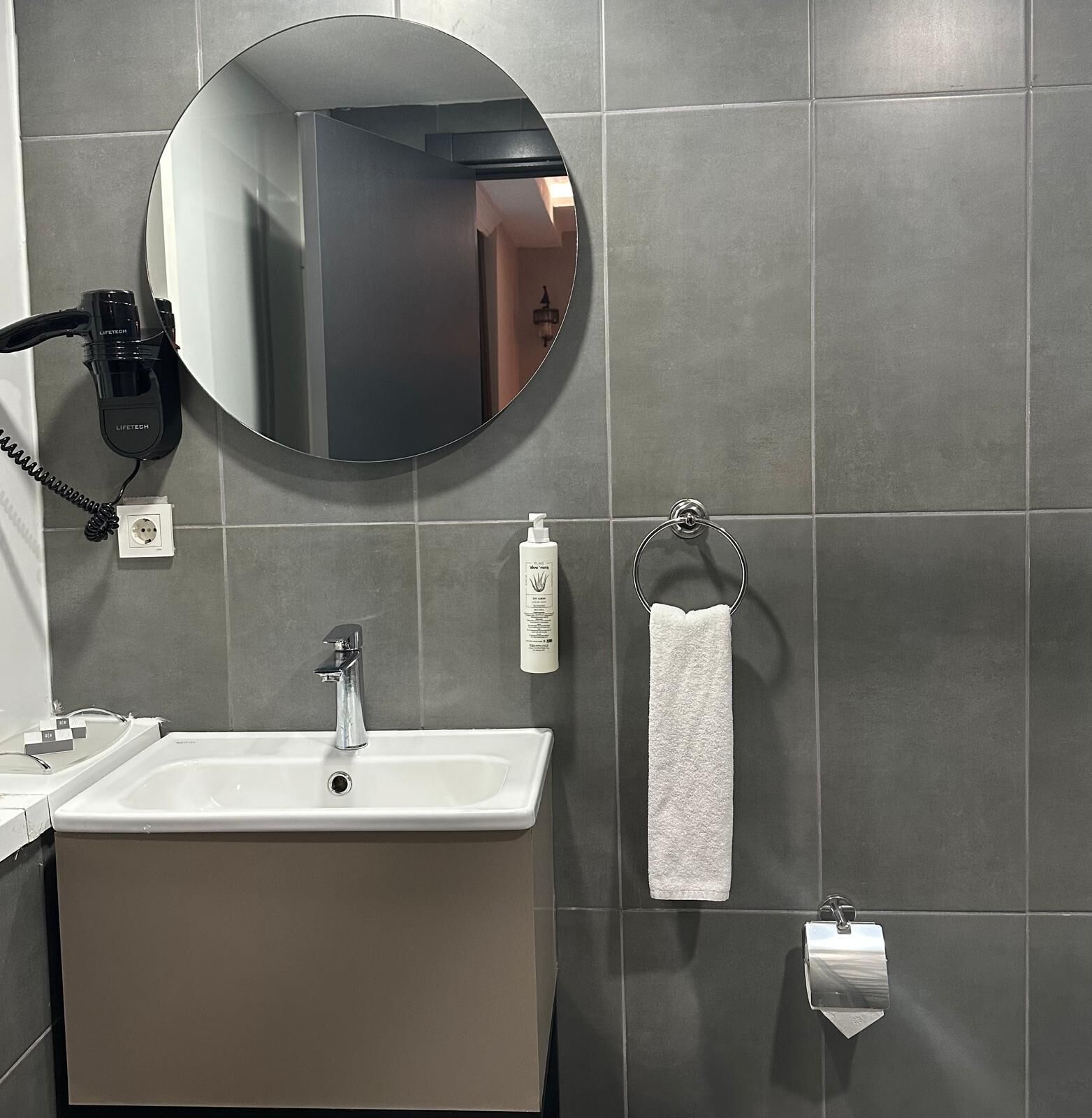 Un baño con un lavamanos blanco, un espejo redondo, un perchero y un secador de pelo.