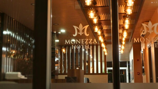 Interior de hotel com uma receção, um candelabro e um letreiro a indicar "MONEZZA HOTEL".