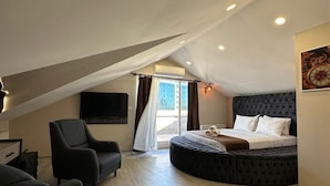 Quarto moderno com uma cama grande, um espaço de estar com duas cadeiras e uma televisão de tela plana fixada na parede.