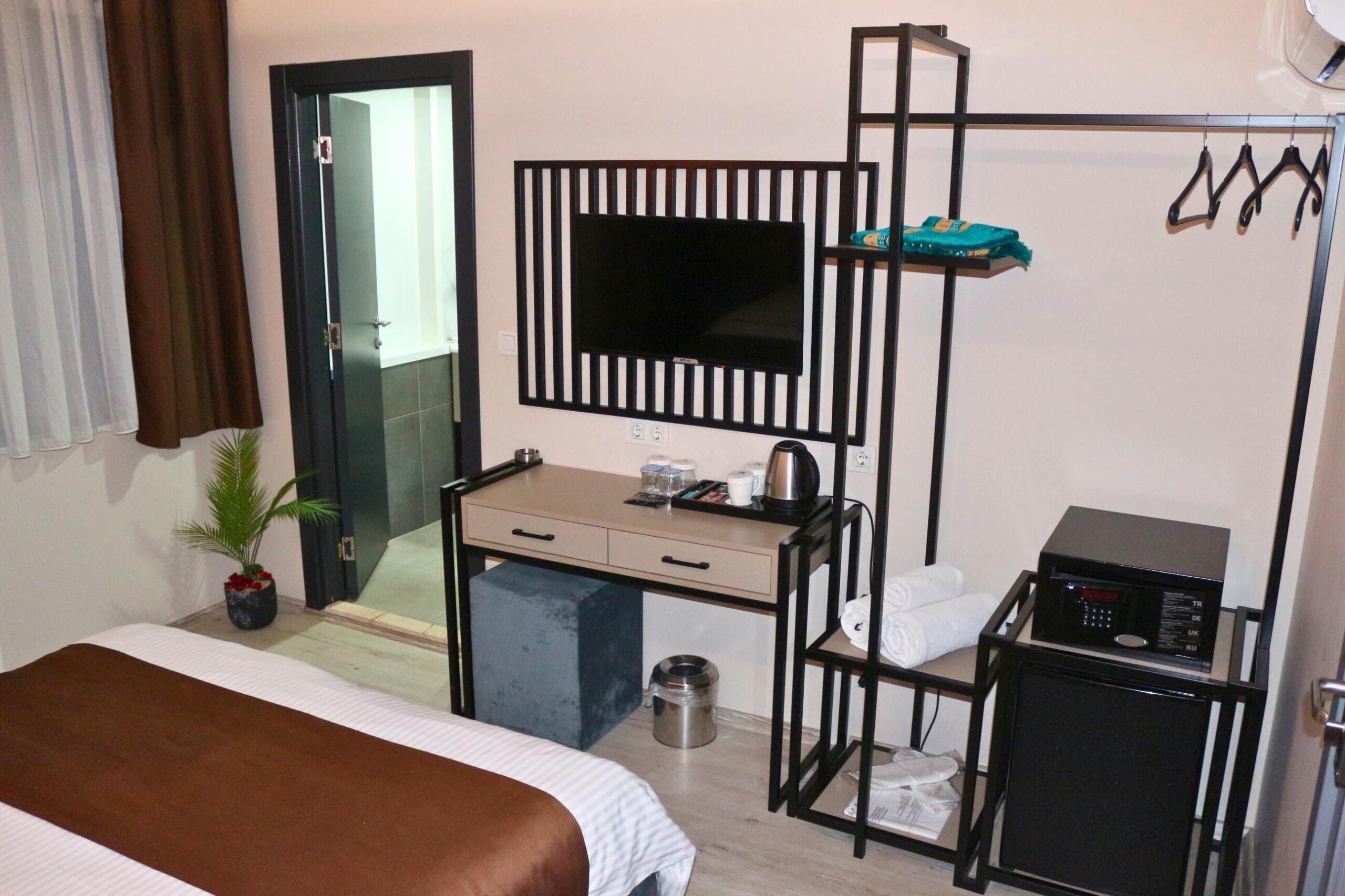 A hotel room with a bed, a desk with a computer, a TV, a microwave, and a small shelf with towels.