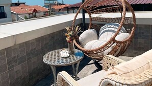 Terraço no telhado com móveis de vime, incluindo uma cadeira suspensa e uma pequena mesa com uma xícara e um vaso.