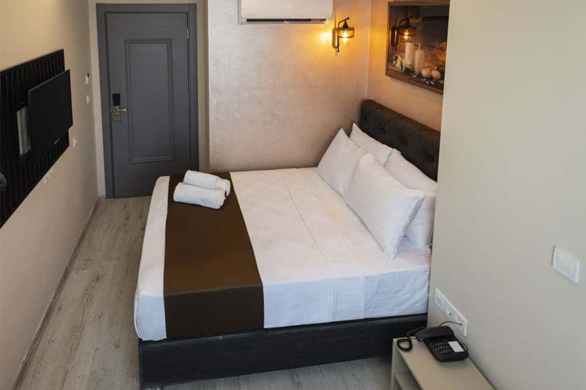 A hotel room with a bed, a bedside table, a wall-mounted air conditioner, and a door.