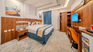 A hotel room with a bed, bedside table, TV, desk, and wardrobe. - Al Marzam Hotel (Madinah)
