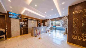 A hotel reception area with a marble counter, a television, and a decorative wall. - Al Marzam Hotel (Madinah)