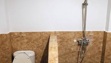 Un baño con inodoro, ducha y pared revestida de mármol.