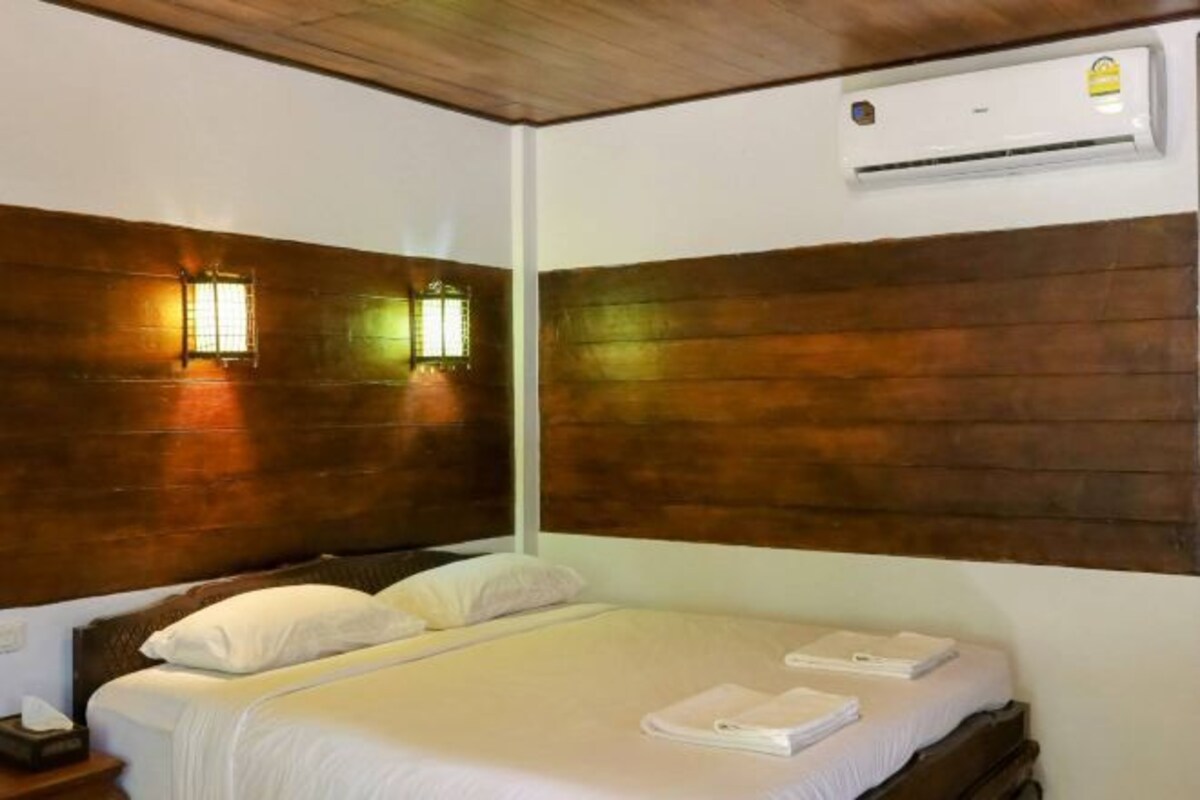 A hotel room with a wooden headboard, a bed with white linens, and an air conditioning unit on the wall.