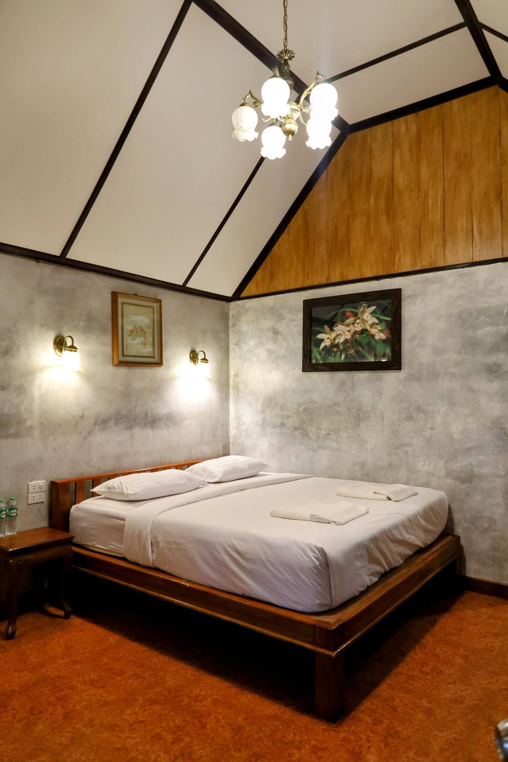 A bedroom with a wooden bed, two wall-mounted lights, a framed picture, and a chandelier.
