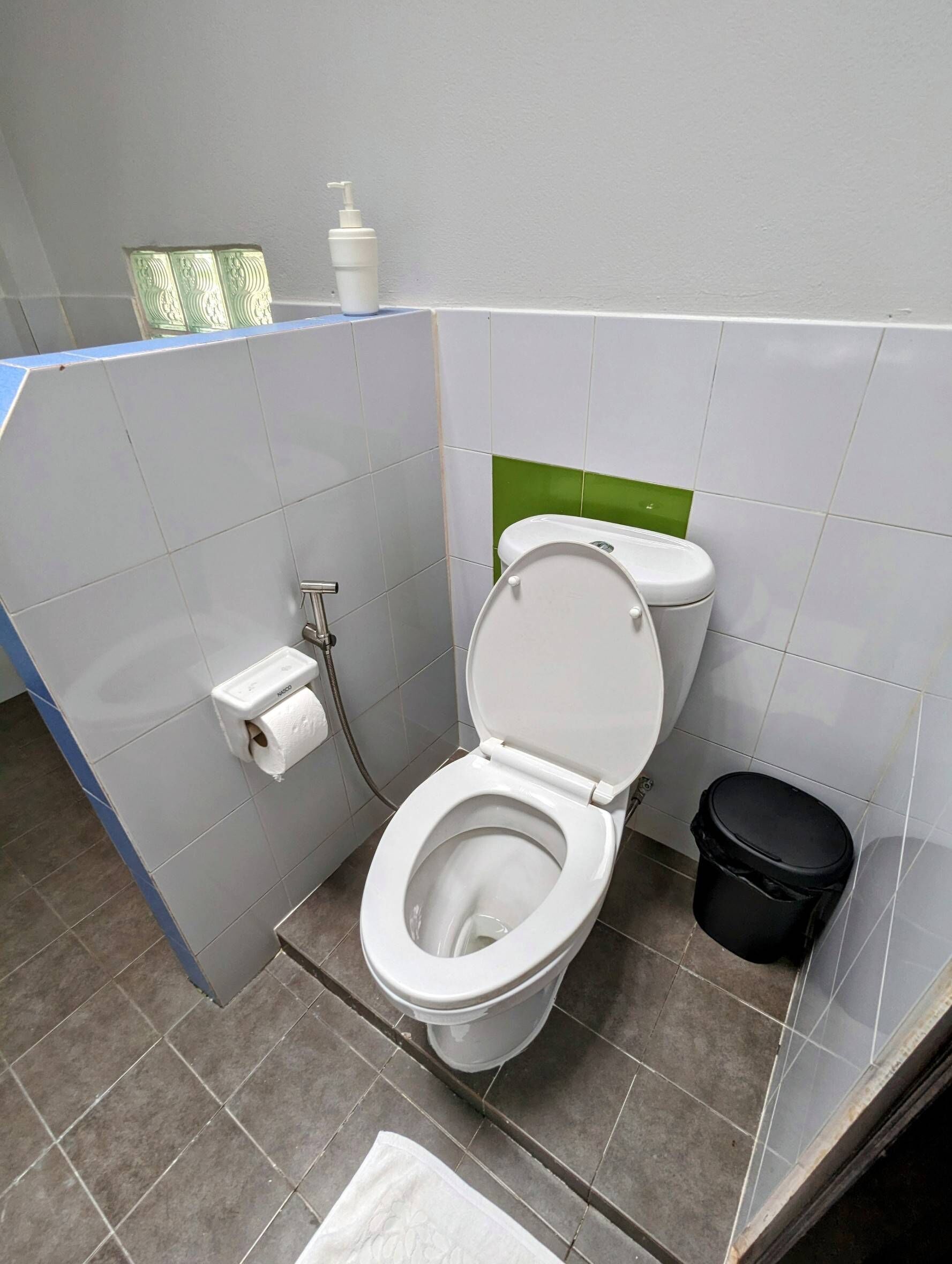 Et standard badeværelse med toilet, håndtørrer, skraldespand og papirhåndklædedispenser.