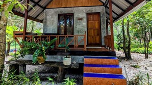 A rustic wooden cabin with a sloped roof, a porch with steps, and a small garden area. - Ziggy Stardust (Ranong)
