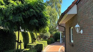A brick pathway leading to a building with a white window and a white lantern on the wall.