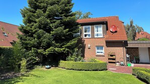 A two-story house with a red-tiled roof, a brick facade, and a large evergreen tree in the front yard.