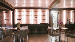 A modern bar area with glass shelving displaying various glassware and bottles, surrounded by wicker chairs and tables. - Villa Grumolara & Spa (Lamezia Terme)