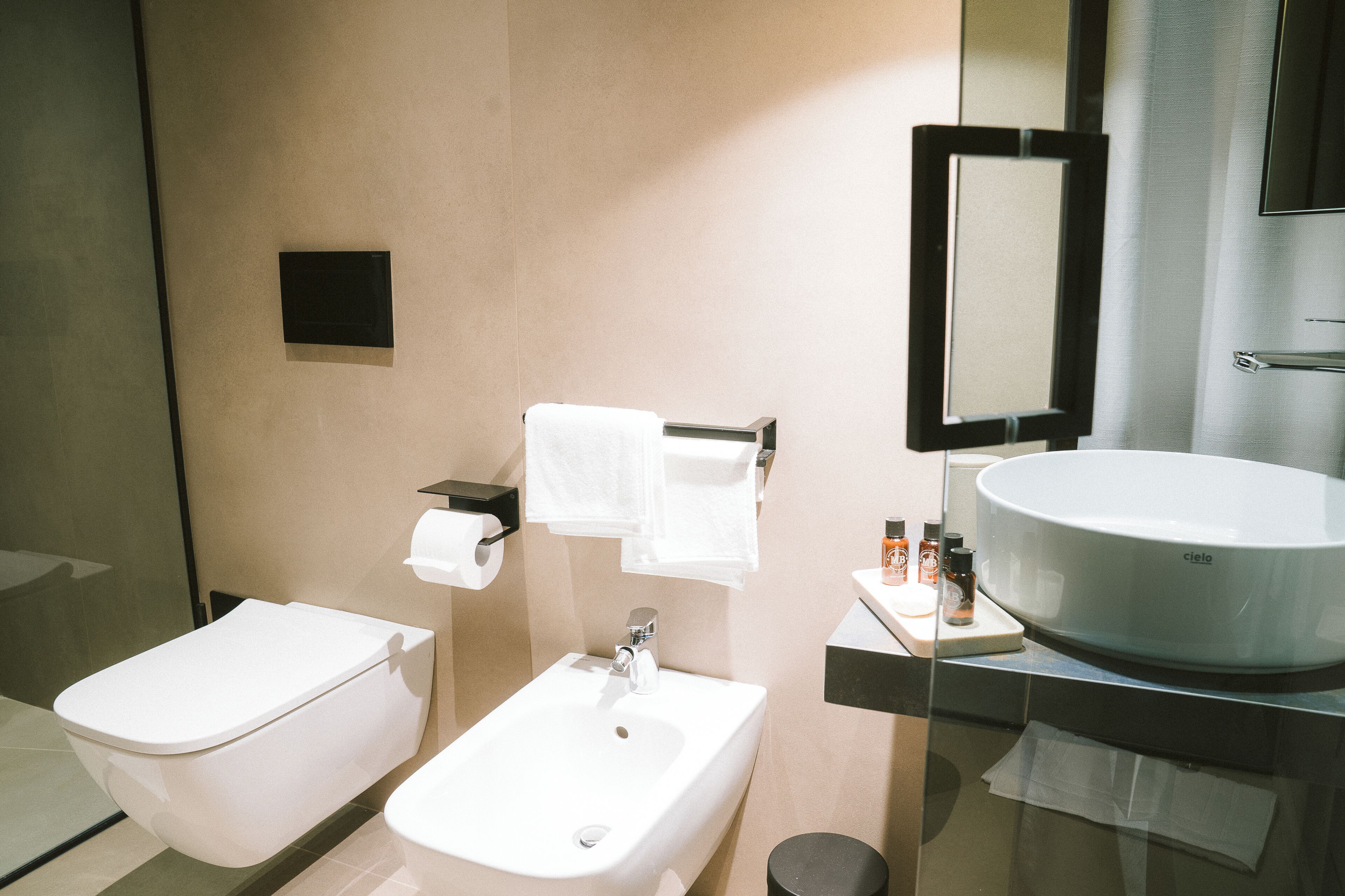 A modern bathroom with a toilet, bidet, sink, and large mirror.