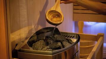 A person pouring a liquid from a wooden ladle into a metal container filled with rocks.