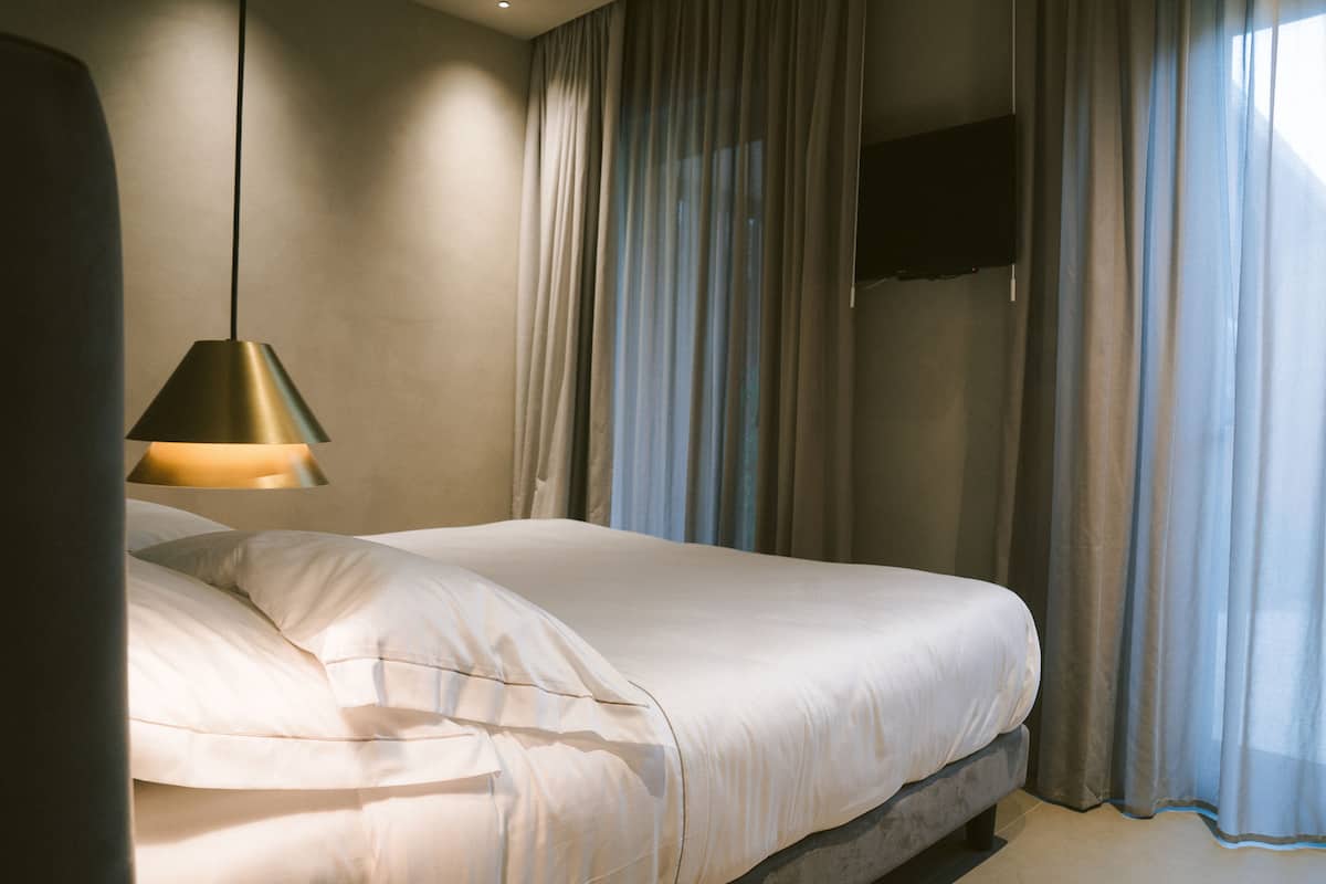 Een slaapkamer met een bed, een hanglamp en een raam met gordijnen.