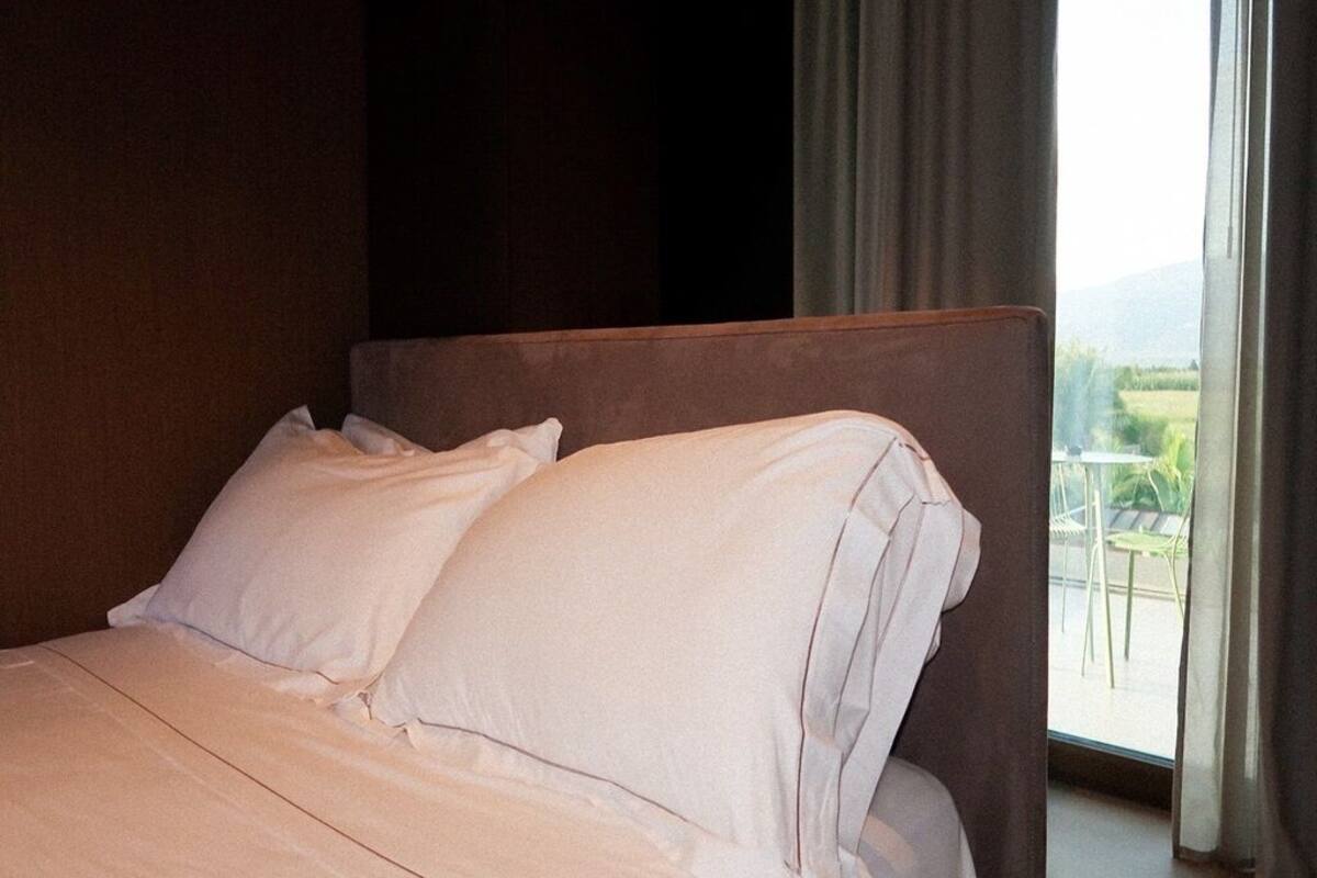 Een hotelkamer met een bed, uitzicht op de natuur door een raam, en een balkon met stoelen.