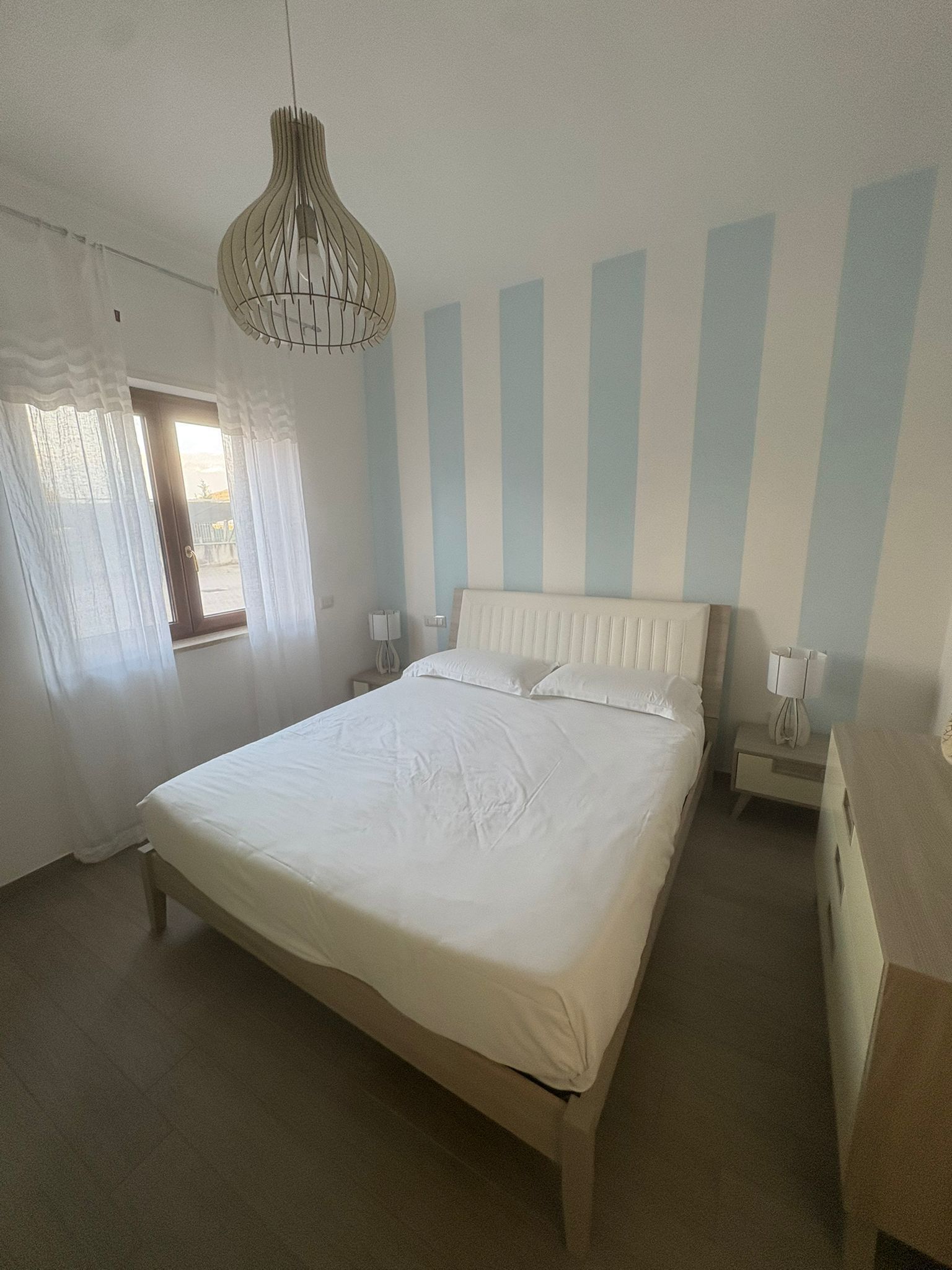 Une chambre avec un grand lit, un luminaire suspendu, une fenêtre avec des rideaux et un radiateur.