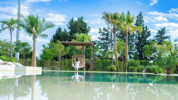 A serene pool area with a swing chair, lush greenery, and a clear sky. - Villa Grumolara & Spa (Lamezia Terme)