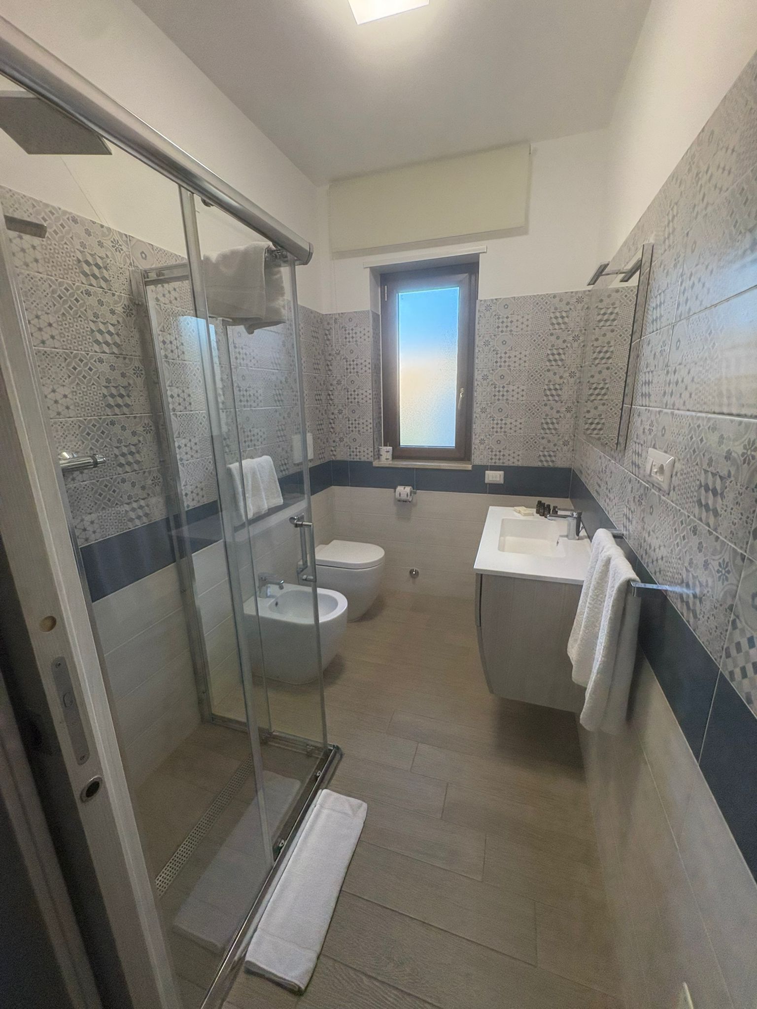 A bathroom with a glass-enclosed shower, two toilets, a sink, and a window.