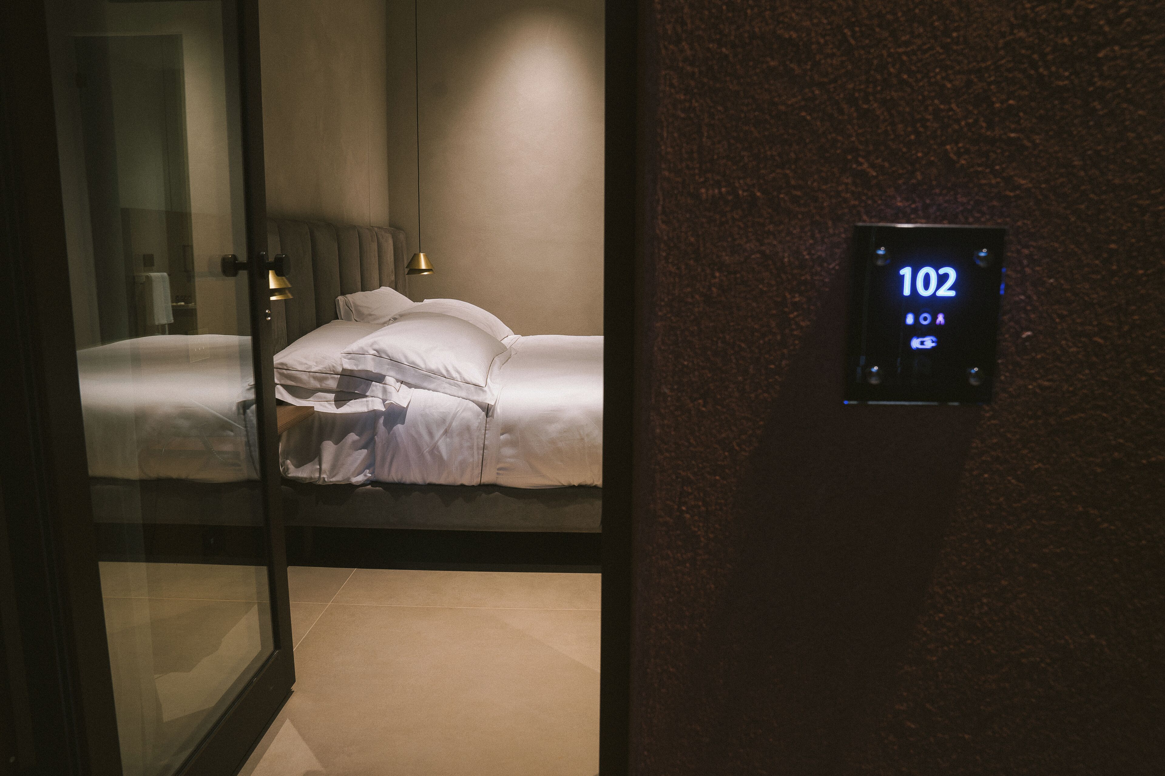 Une chambre d’hôtel équipée d  ’un lit, d’une table de chevet et d’un écran numérique fixé au mur, affichant le numéro de chambre : 102.