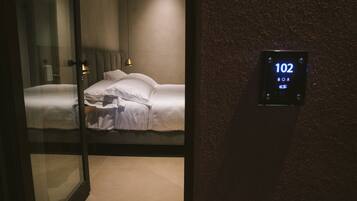 Hotelkamer met een bed, nachtkastje en een aan de muur bevestigd scherm dat kamer nummer 102 toont.
