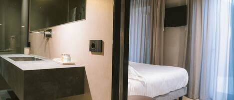 A modern hotel room with a large bathroom sink, a bed, and a flat-screen TV mounted on the wall.
