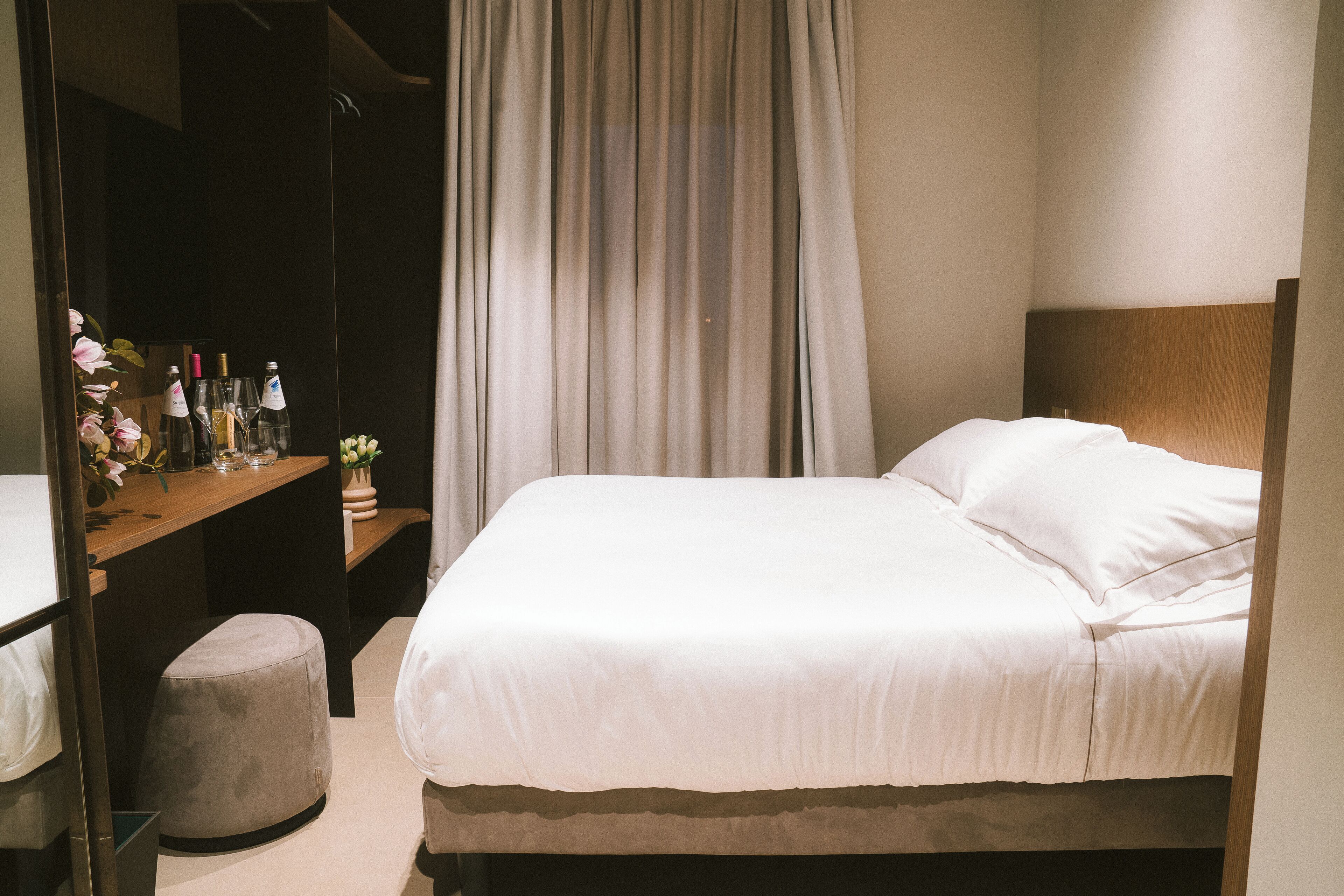 Een keurig opgemaakt slaapkamer met een bed, een nachtkastje met flessen en een klein krukje.