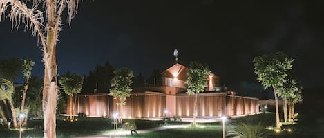 A modern building with a dome and a weather station on top, surrounded by well-lit pathways and greenery.
